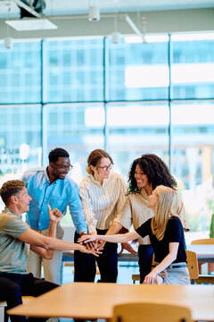Diverse business people stacking hands, symbolizing teamwork, partnership, and unity in a modern office environment