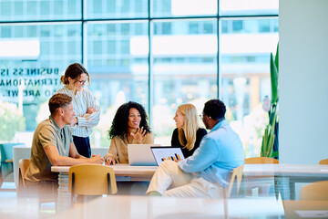 Naklejka na ściany i meble Multiracial business professionals discussing project during informal meeting in contemporary workplace with open plan design