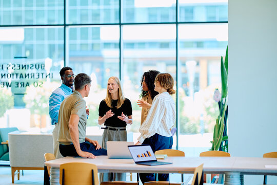 Group of multi-ethnic colleagues engaged in discussion and teamwork, standing in a contemporary workplace with glass walls