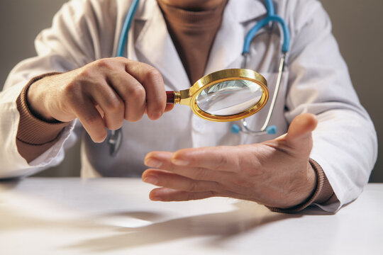 Doctor holding a magnifying glass and examining a patient's hand.