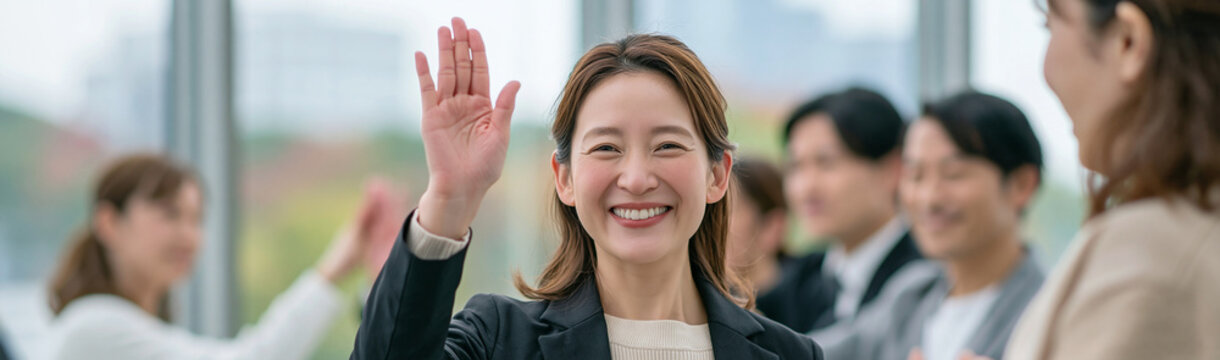Engaged Participant: A cheerful woman raises her hand in a meeting, eager to share her thoughts, with colleagues in the background.