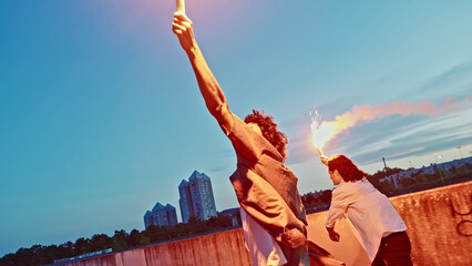 A skateboarder, young and full of energy, stands on a rooftop, holding a torch high in hand, the flame casting a warm glow against the twilight sky. © wkproduction