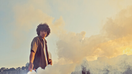 A skateboarder in adolescence stands against a dramatic sky, smoke billowing around him representing youth culture and carefree lifestyle. © wkproduction