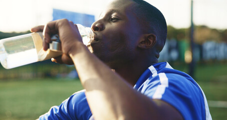 Obraz premium Soccer, break and black man with drinking water for hydration, wellness and training outdoor. Football, thirsty and sports person or player with liquid bottle, resting and practice on field for game