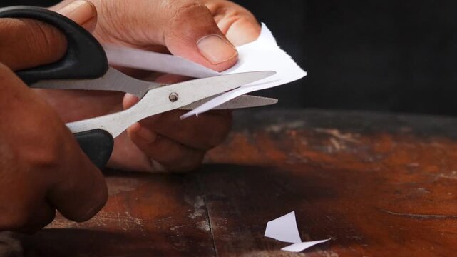 A man's hand cuts a sheet of white paper with scissors and cuts off the corners. Close-up, DIY concept.