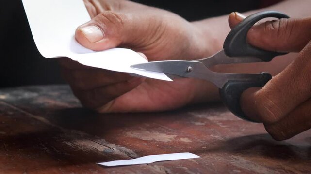 A man's hand cuts a sheet of white paper with scissors and cuts off the corners. Close-up, DIY concept.