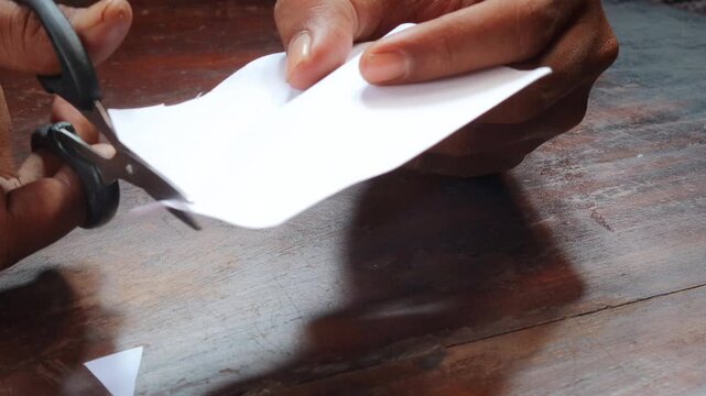 A man's hand cuts a sheet of white paper with scissors and cuts off the corners. Close-up, DIY concept.