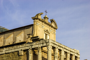 The Temple of Antoninus and Faustina in Rome, Italy, with its ancient Roman columns and frieze, stands against a clear blue sky, showcasing its historical significance and architectural beauty. © Nick