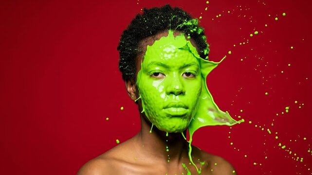 Vibrant green paint splashes across a person's face in a dynamic studio portrait. A striking visual of bright green liquid exploding and dripping onto a person's head and shoulders