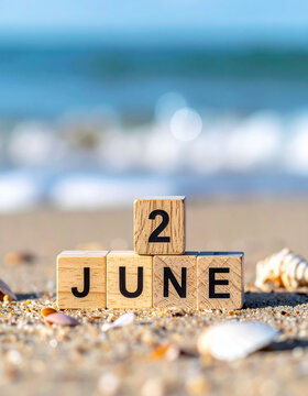 Wooden cubes with text 2 June on sandy beach, blurred seashells and coastal elements, ocean waves on background, vacation planning and summer trip reminder concept. Close-up.