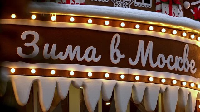 Moscow, December 30 2025, Close-up of a sign reading Winter in Moscow. White text on brown background with snow-icing details. Warm string lights highlight the festive message. Ideal for holiday