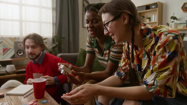 Low angle shot of two girls laughing while looking through camera pictures during relaxing, friendly evening with drinks and board games