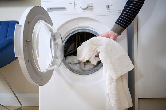 Close-up of a man putting dirty towel into the washing machine.