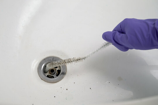 A man cleans the drain hole in a Jacuzzi bathtub with a brush.