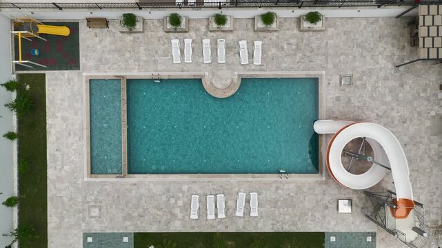 Aerial Video of outdoor pool with aqua slide and empty loungers in resort courtyard
