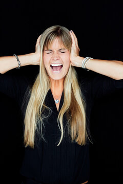 Portrait of screaming blond woman with head in hands in front of black background