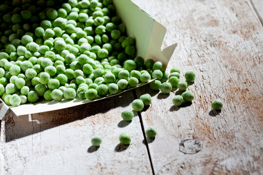 Opened package of deep frozen peas on wood