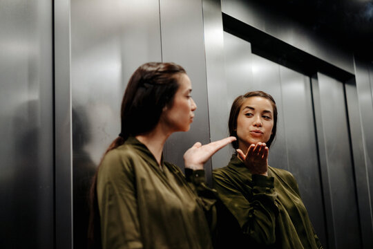 Young woman looking in mirror in elevator blowing a kiss