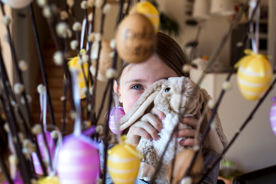 Girl hiding behind Easter bunny and twigs of willows decorated with Easter eggs