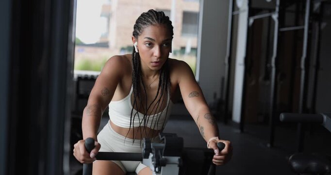 Athletic woman with braided hair and tattoos intensely working out on a stationary exercise bike, building stamina and endurance during a cardiovascular training session in a modern fitness center