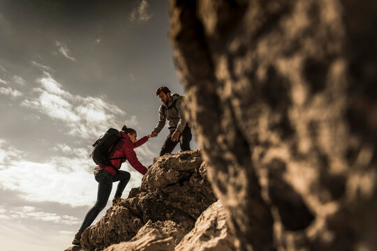 Germany, Bavaria, Oberstdorf, man helping woman climbing up rock