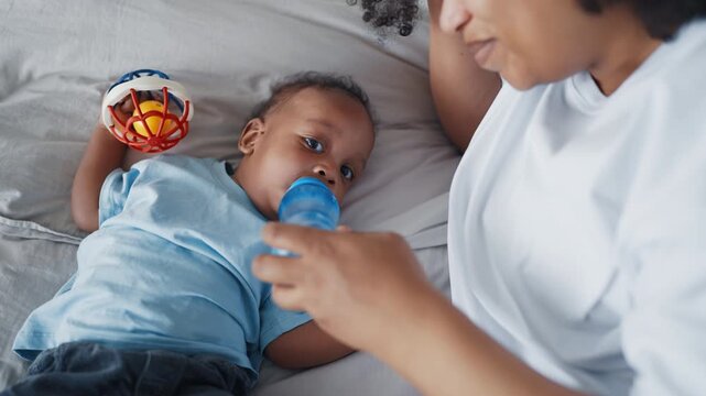 Formula feeding for healthy infant, mother holding little bottle with water. Family and motherhood, african american woman spending time with her little baby at home, carefree childhood and parenting
