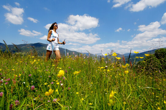 Young woman Nordic walking in meadow, Germany, smiling, low angle view