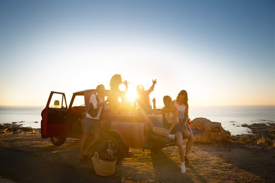 Happy young people outside pick up truck at the coast at sunset