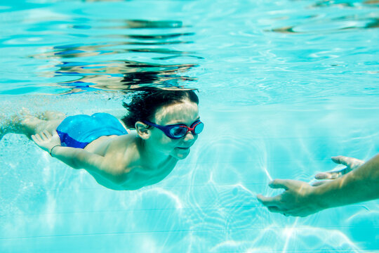 Young boy diving to mother, under water, swimming pool