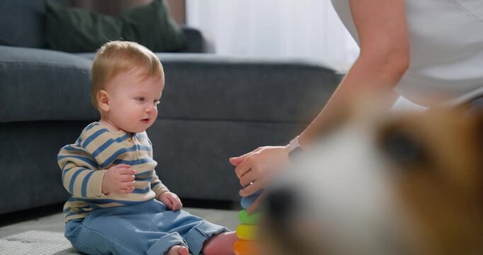 Young toddler playing with colorful stacking rings toy on floor, engaging in early childhood development and sensory play while caregiver encourages learning at home