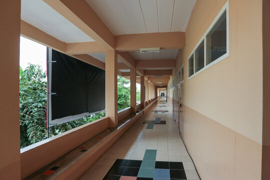 Perspective view of a long open corridor inside a school building with tiled flooring.