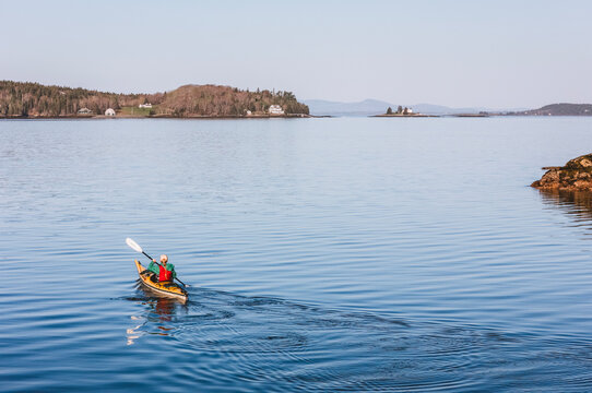 woman kayaking alone on a calm blue sea along the Maine coast.