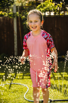 Happy child playing in backyard sprinkler on sunny summer day
