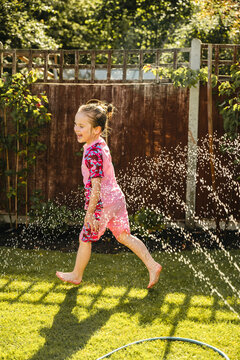 Joyful child running through garden sprinkler in summer backyard