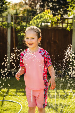 Happy child playing in backyard sprinkler on sunny summer day