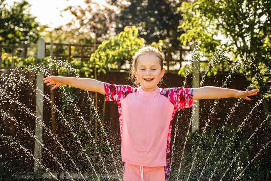 Happy child playing in backyard sprinkler on sunny summer day