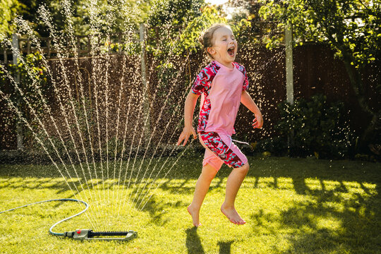 Joyful child running through garden sprinkler in summer backyard