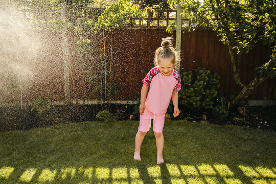 Happy child playing in backyard sprinkler on sunny summer day