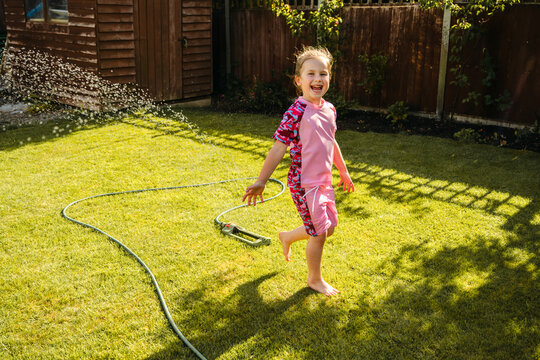 Joyful child running through garden sprinkler in summer backyard