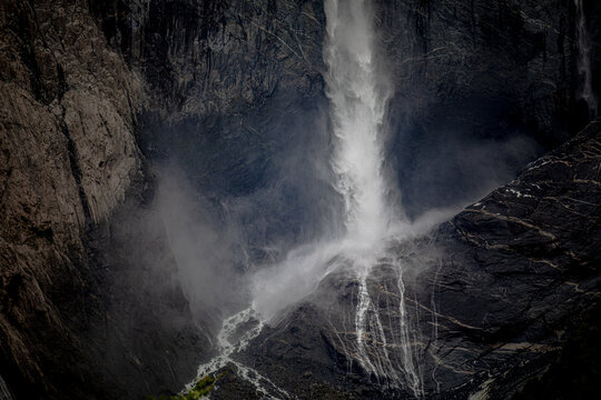 Misty waterfall crashes against dark rugged cliffs