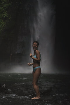 Joyful woman laughing in river by misty waterfall, Sekumpul, Bali