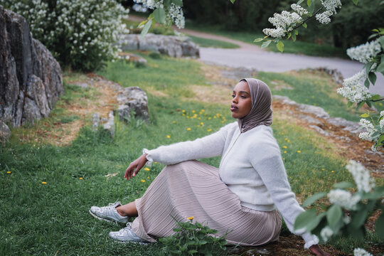 Young Muslim woman in hijab relaxing under blooming spring trees