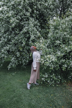 Muslim woman standing beneath blooming spring tree in green garden