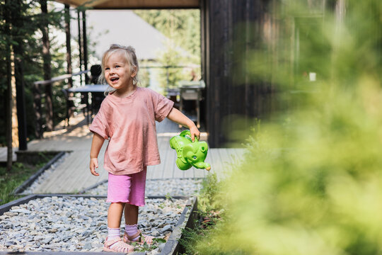 Cute toddler girl watering plants in the backyard