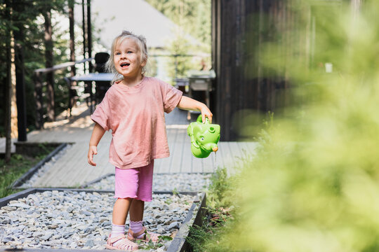 Cute toddler girl happily watering plants outside