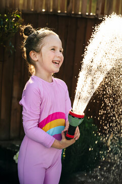 Joyful child holding garden water hose in backyard in summer sunlight