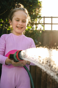Joyful child holding garden water hose in backyard in summer sunlight