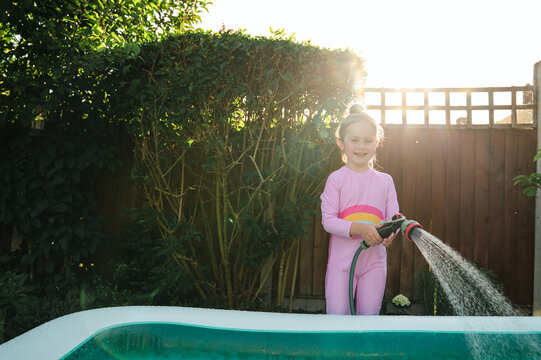 Child filling inflatable pool in sunny backyard, summer holiday