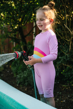 Happy, smiling child watering backyard in summer sunlight
