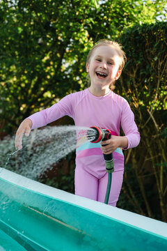 Joyful child watering backyard in summer sunlight